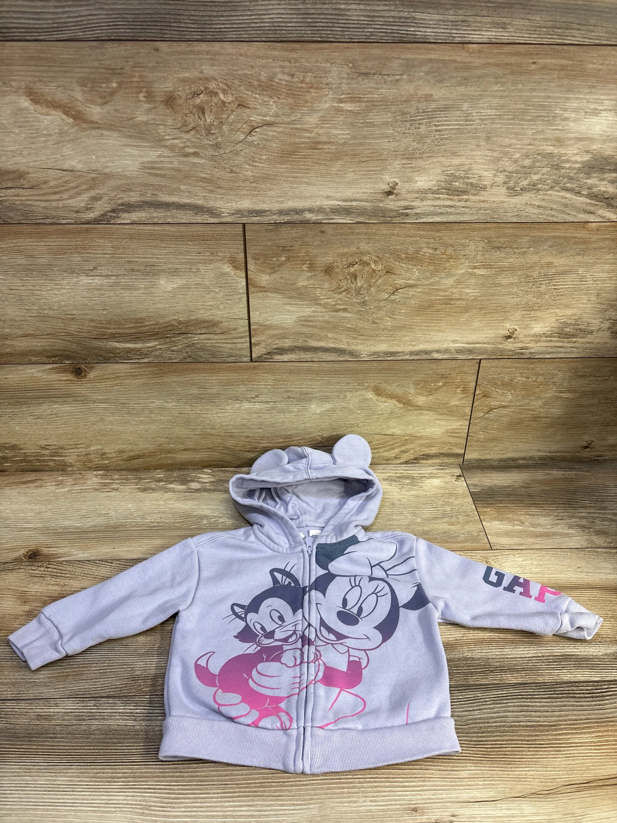 Front view of a lilac Minnie Mouse full-zip hooded sweatshirt with character graphics and rounded-ear hood on wood flooring