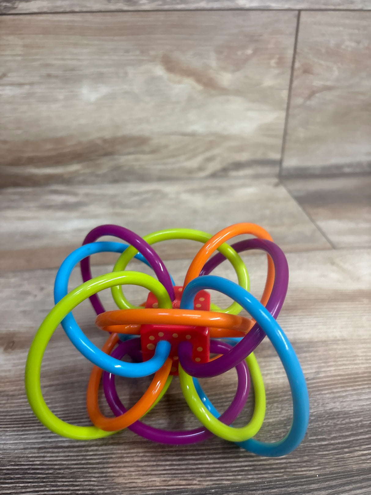 Colorful baby teething toy with interlocking loops in blue, purple, orange, and green on wood floor