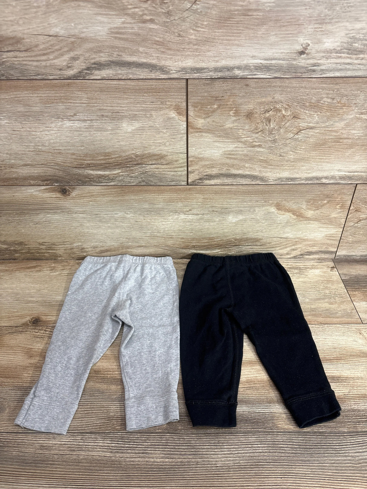 Flat lay of Carter's 2-pack 12M pull-on pants, gray and black, showing elastic waists and cuffed ankles on wood