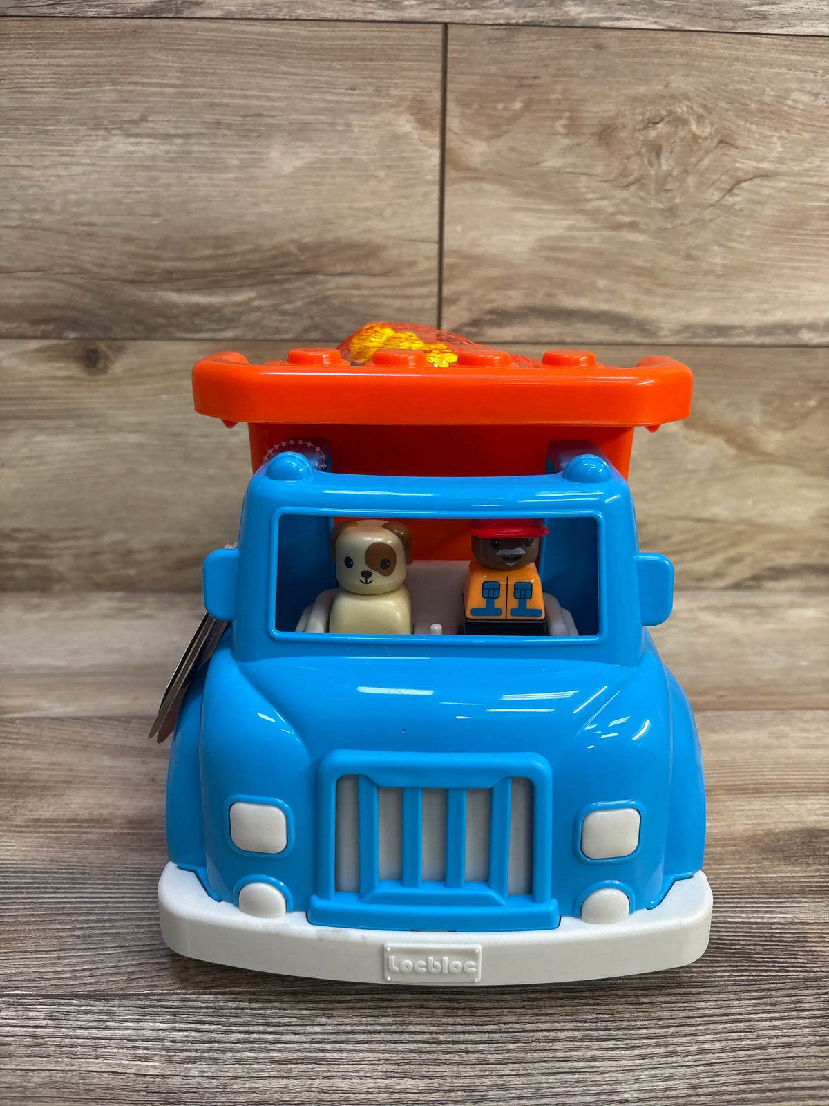Front view of Battat dump truck with building blocks 17pc showcasing dog and construction worker figures with wood-look background
