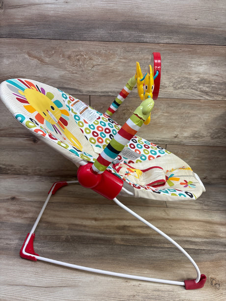 Angled view of Bright Starts Playful Pinwheel Vibrating Baby Bouncer showcasing colorful patterned seat, toy bar, and white-and-red frame on wood floor