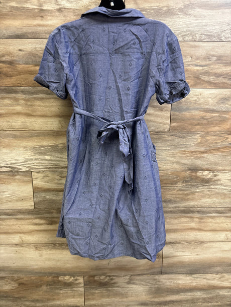 Back view of blue chambray shirtdress with tied waist bow, rolled short sleeves, subtle diamond print on wood background
