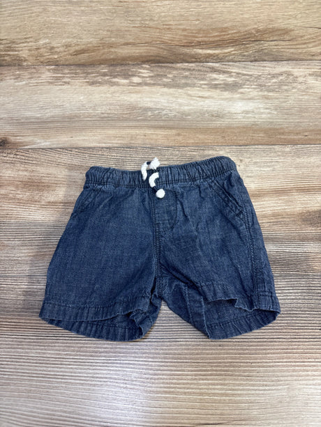 Flat lay of Jumping Beans chambray baby shorts in blue, size 6M, showing drawstring waistband and side pockets on wood background