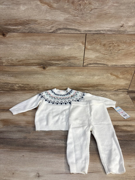 White knit baby sweater and pants set with geometric pattern on wooden background