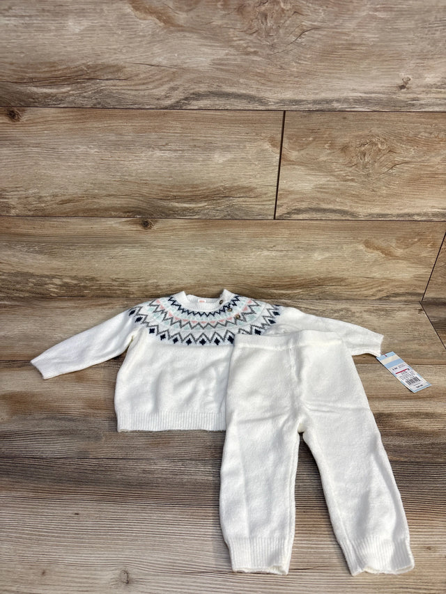 White knit baby sweater and pants set with geometric pattern on wooden background