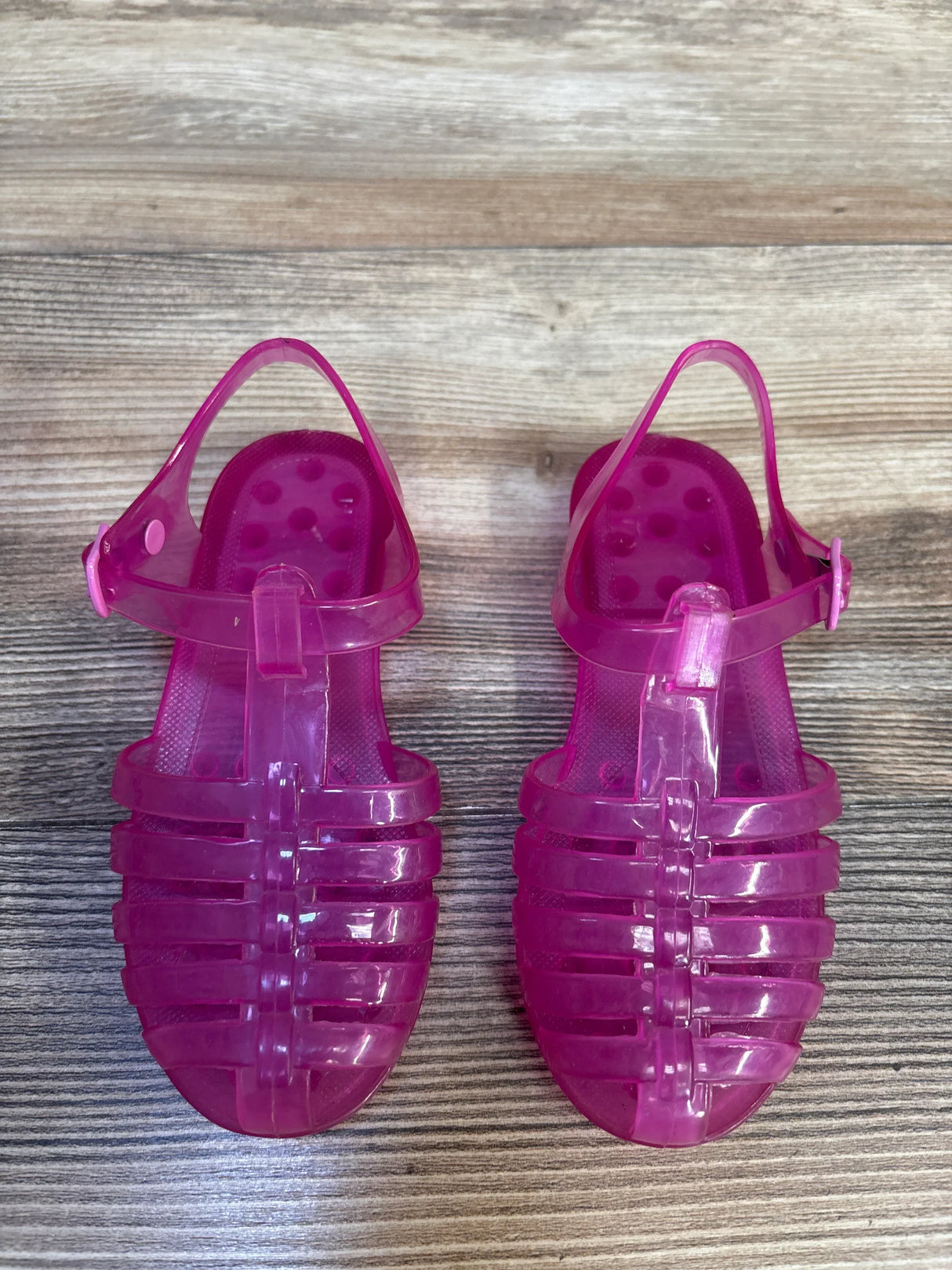 Top down view of Janie and Jack pink jelly fisherman sandals size 9C showing translucent strappy upper and ankle buckle on wood floor