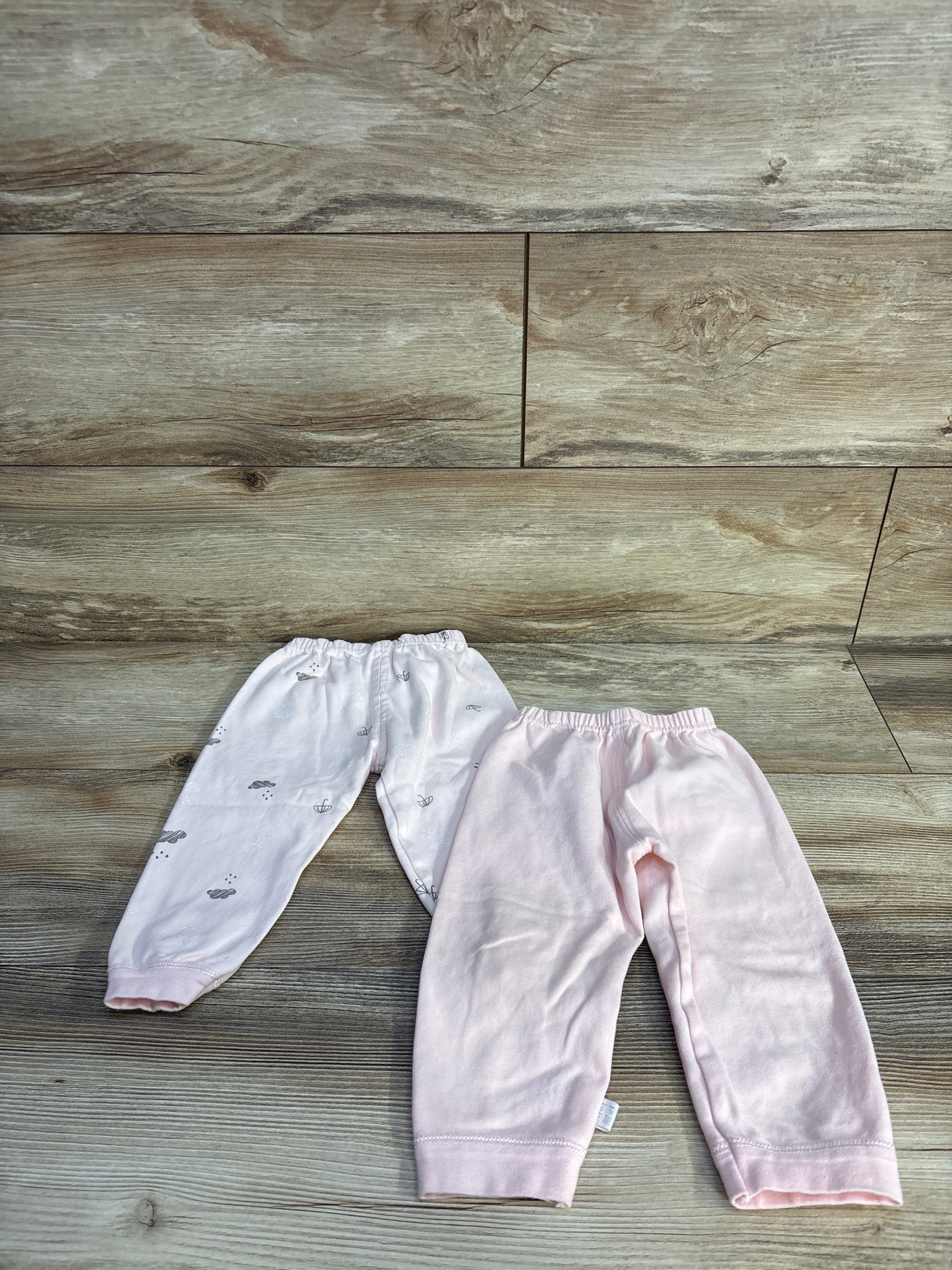 Flat lay of two baby pull-on pants, light pink and white with gray cloud print, with elastic waist and ankle cuffs on wood