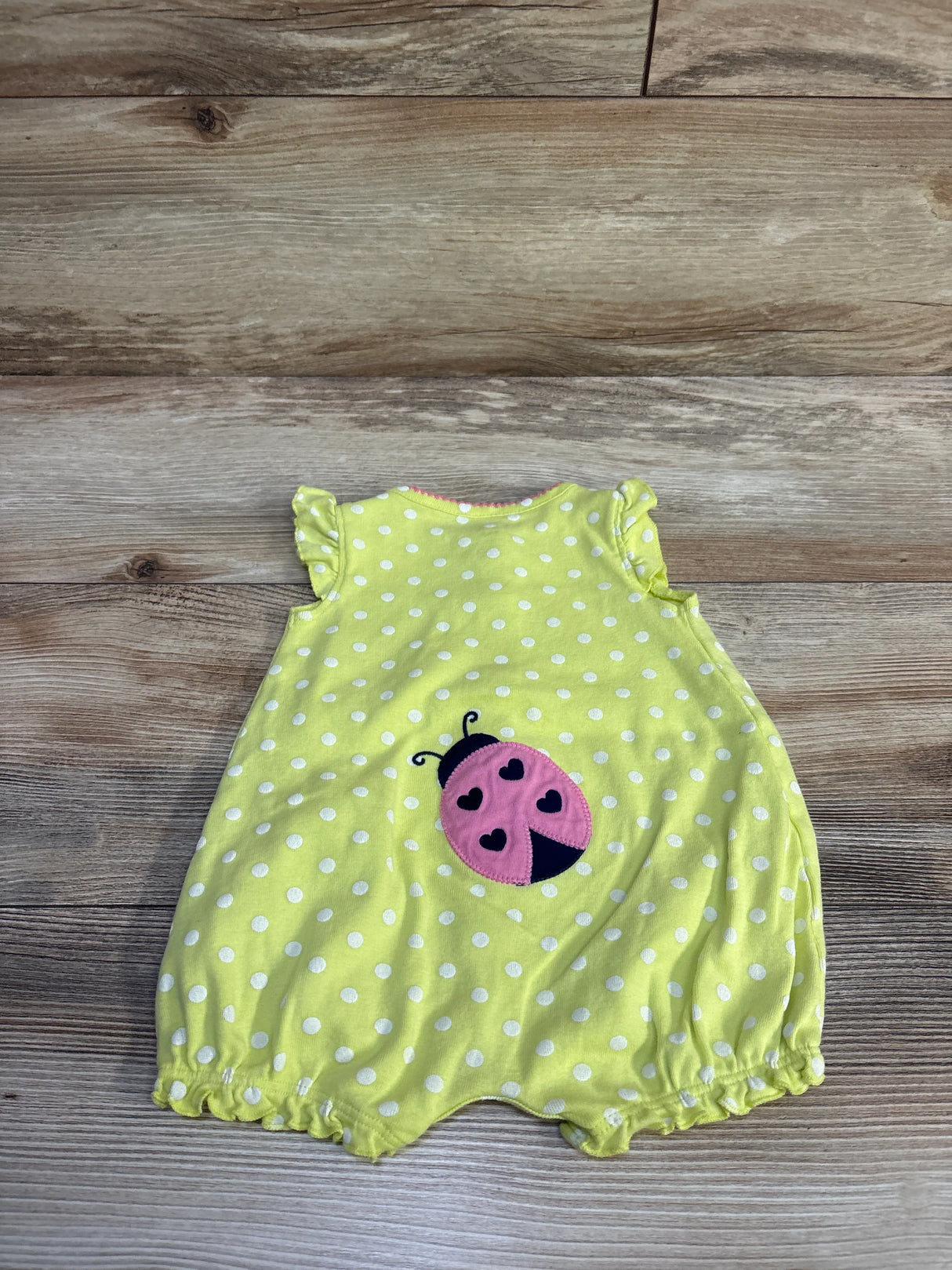 Flat lay of baby shortie romper showing lime yellow fabric with white polka dots and pink ladybug applique on wood background