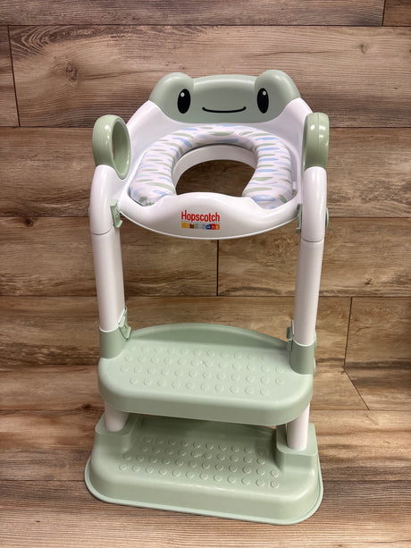 Front view of Hopscotch Lane My First Potty with frog design, padded patterned seat, and two-step platform on wood floor