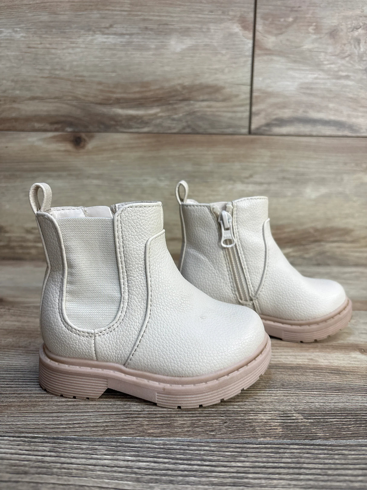 Side view of Cat & Jack Chelsea toddler boots in beige showcasing side zipper and pink sole on wood floor