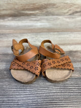 Brown toddler sandals with floral cutout design on wooden background