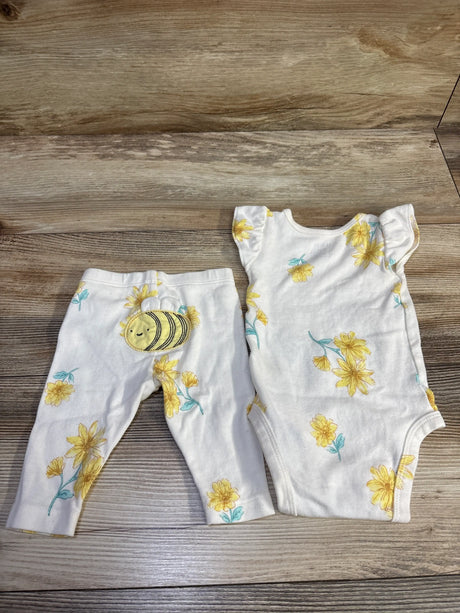 Front view of Carters two piece bodysuit and pants, 3 month size, with white fabric, yellow flowers, bee patch, and wood grain background