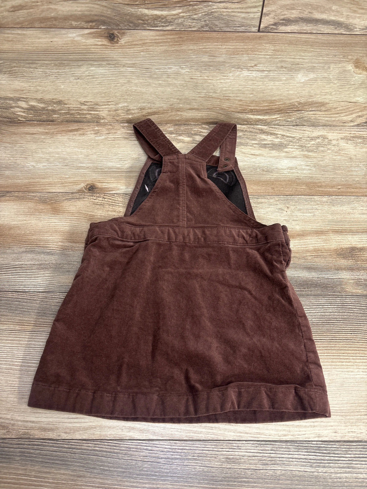Brown corduroy toddler pinafore dress with adjustable straps on wooden floor