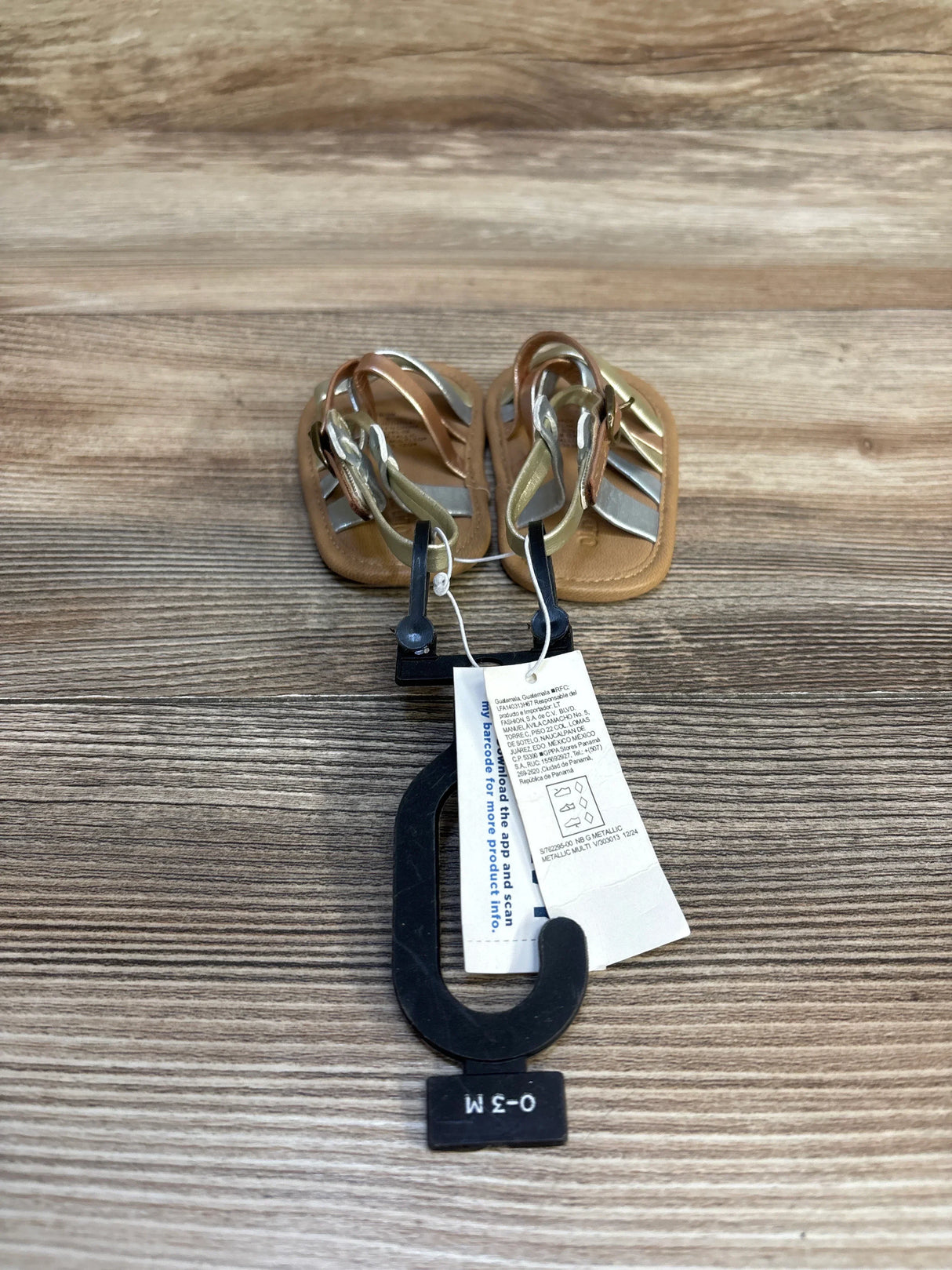 Infant sandals 0-3 months with metallic straps on wood background, resale baby shoes
