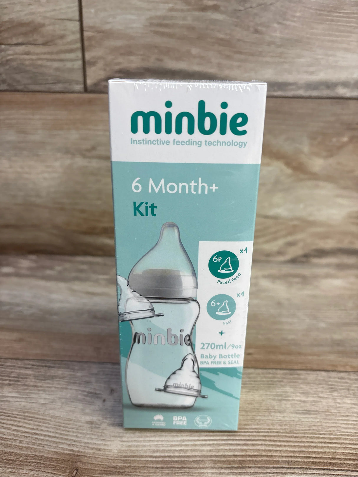 Front view of Minbie 6 Month+ feeding kit box showing 270 ml baby bottle and two teats on a wooden surface background