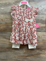 Front view of toddler 2-piece pink smocked floral dress and white leggings set showcasing smocked bodice, ruffle sleeves and ivory bow on wooden background