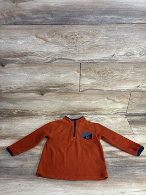 Orange fleece long sleeve kids pullover with blue bear patch and half zip, laid flat on wood