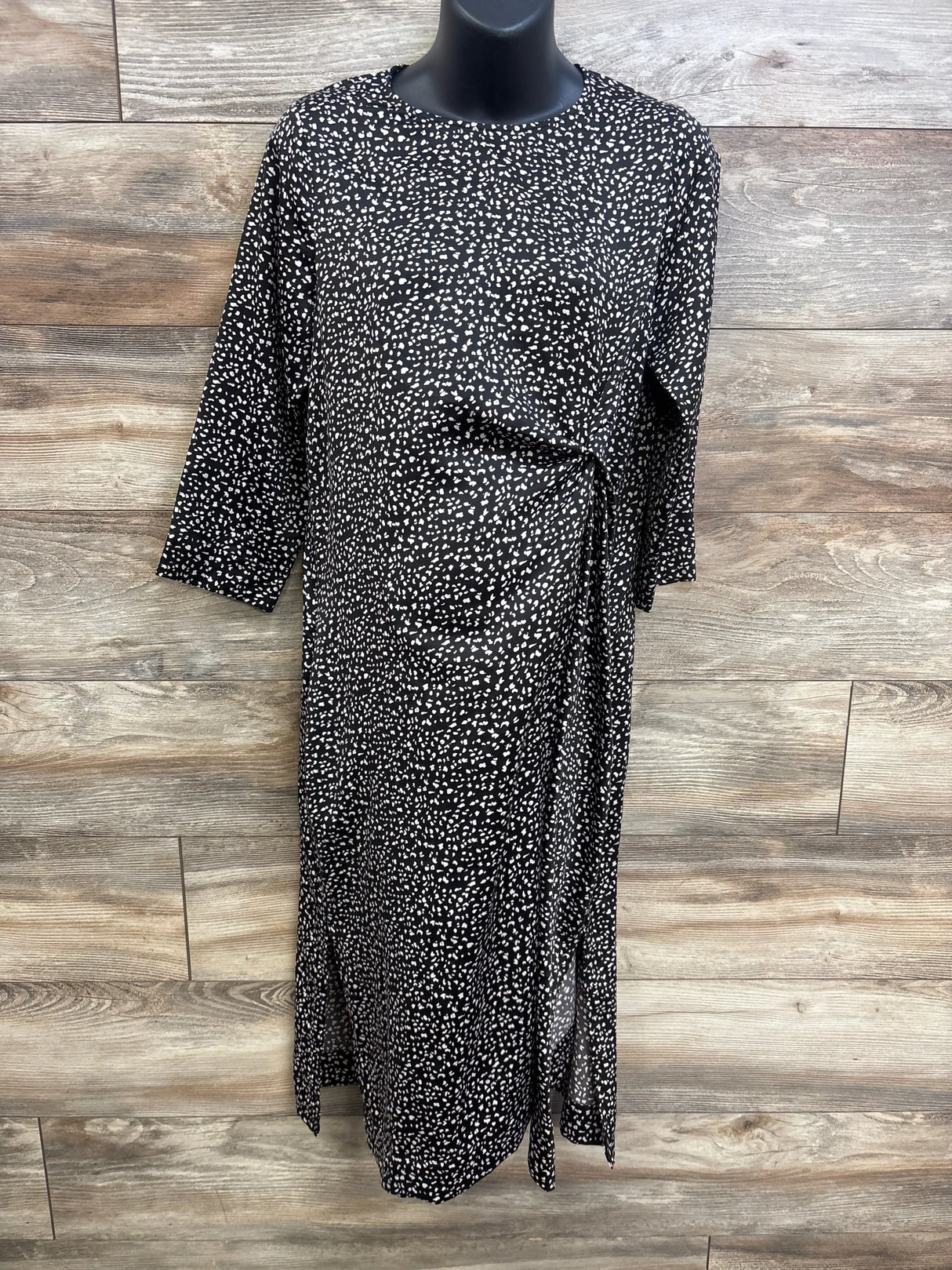 Front view of Hatch Maternity The Lauren dress in black speckle showcasing side tie and 3/4 sleeves on wood background