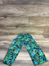 Flat lay of teal tropical print swim cover up pants showing elastic waistband and ruffled ankle hems on wood background