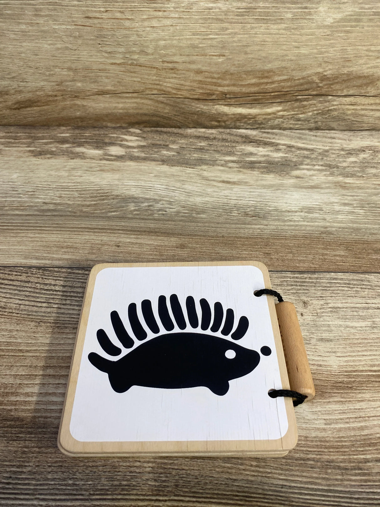 Top-down view of Lovevery wooden board book showing black hedgehog silhouette on white cover and wooden handle on light wood background