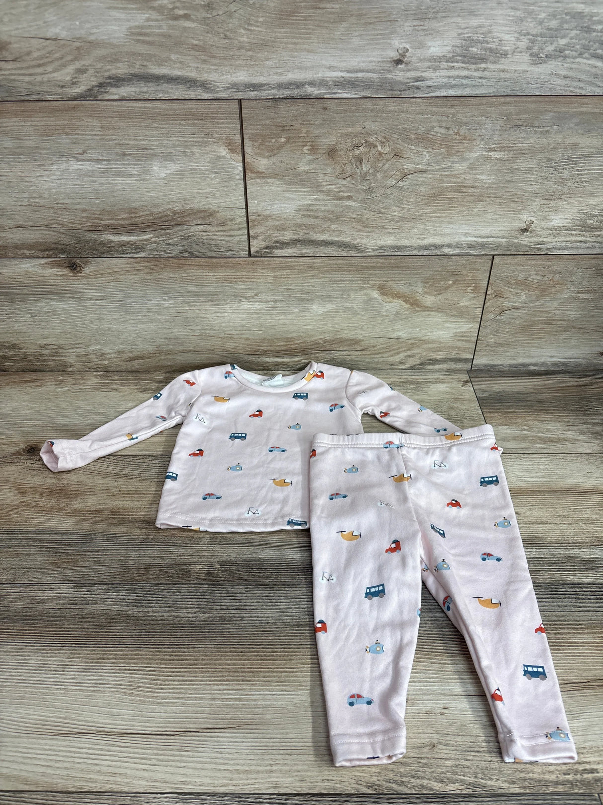 Flat lay of pink 2-piece pajama set showing long-sleeve top and leggings with multicolor vehicle print on wood background