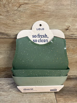 Front view of Lalo 2-pack silicone bibs in sage showing speckled top bib and deep crumb-catching pocket on wood background