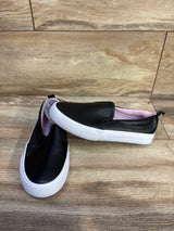 Front-quarter view of Cat & Jack Hailey toddler slip-on sneakers, black faux leather with white rubber sole and pink lining on wood floor