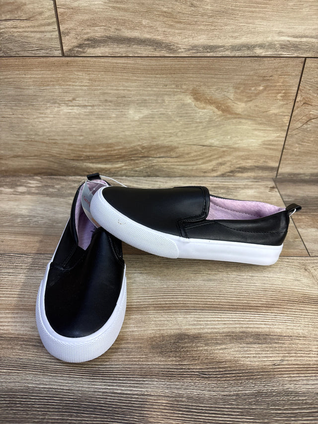 Front-quarter view of Cat & Jack Hailey toddler slip-on sneakers, black faux leather with white rubber sole and pink lining on wood floor