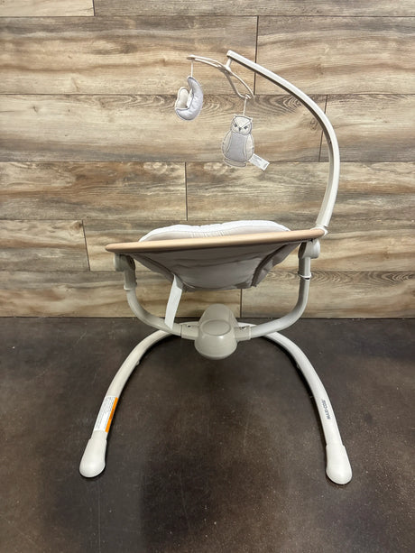 Front view of Maxi-Cosi Cassia Baby Swing in Classic Oat showcasing its wooden tray and hanging owl toy with a wood floor background