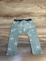 Green baby pants with white palm tree print and black waistband, laid on wood floor