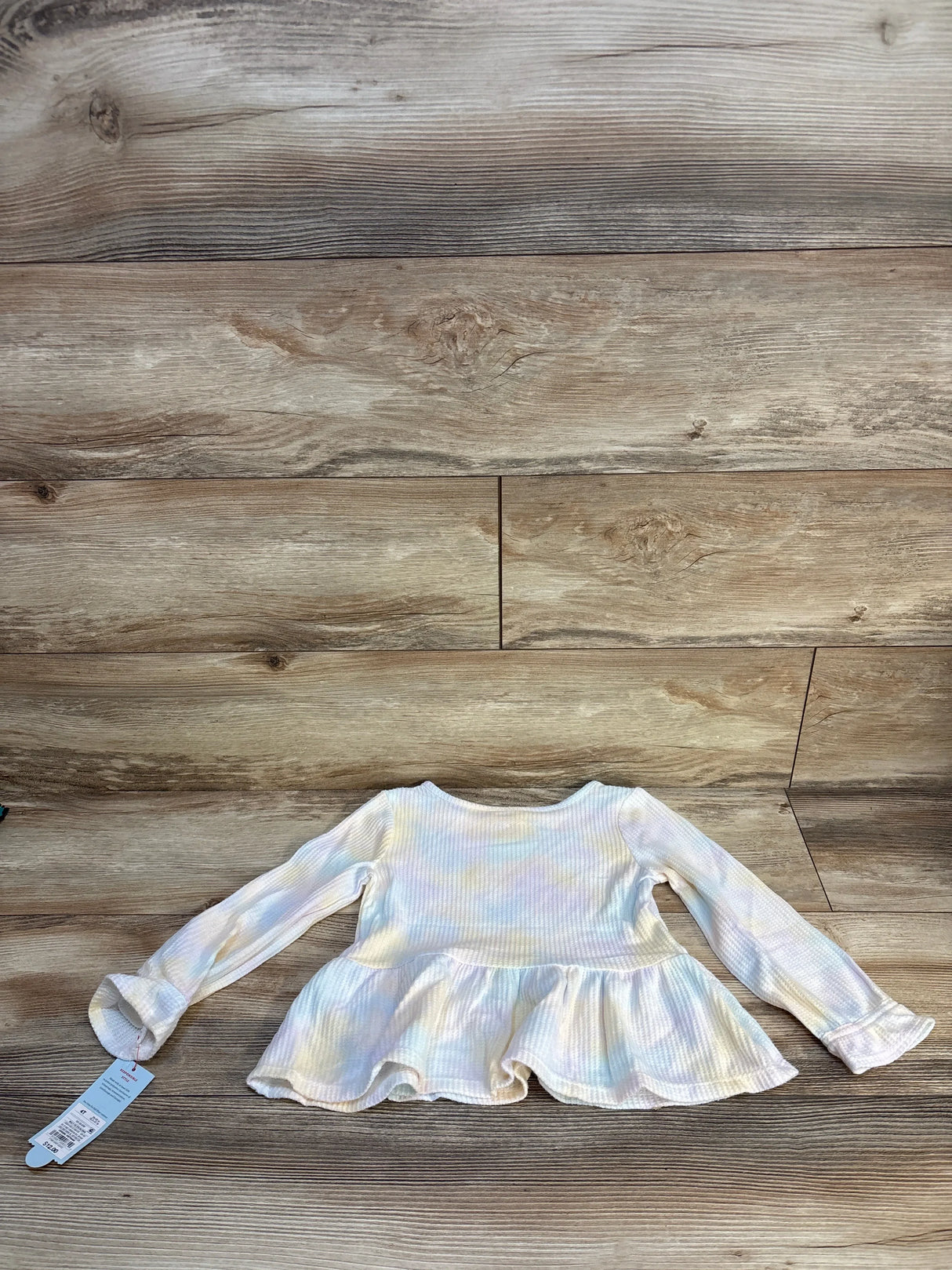 Long sleeve pastel tie-dye toddler shirt with ruffled hem on wooden background