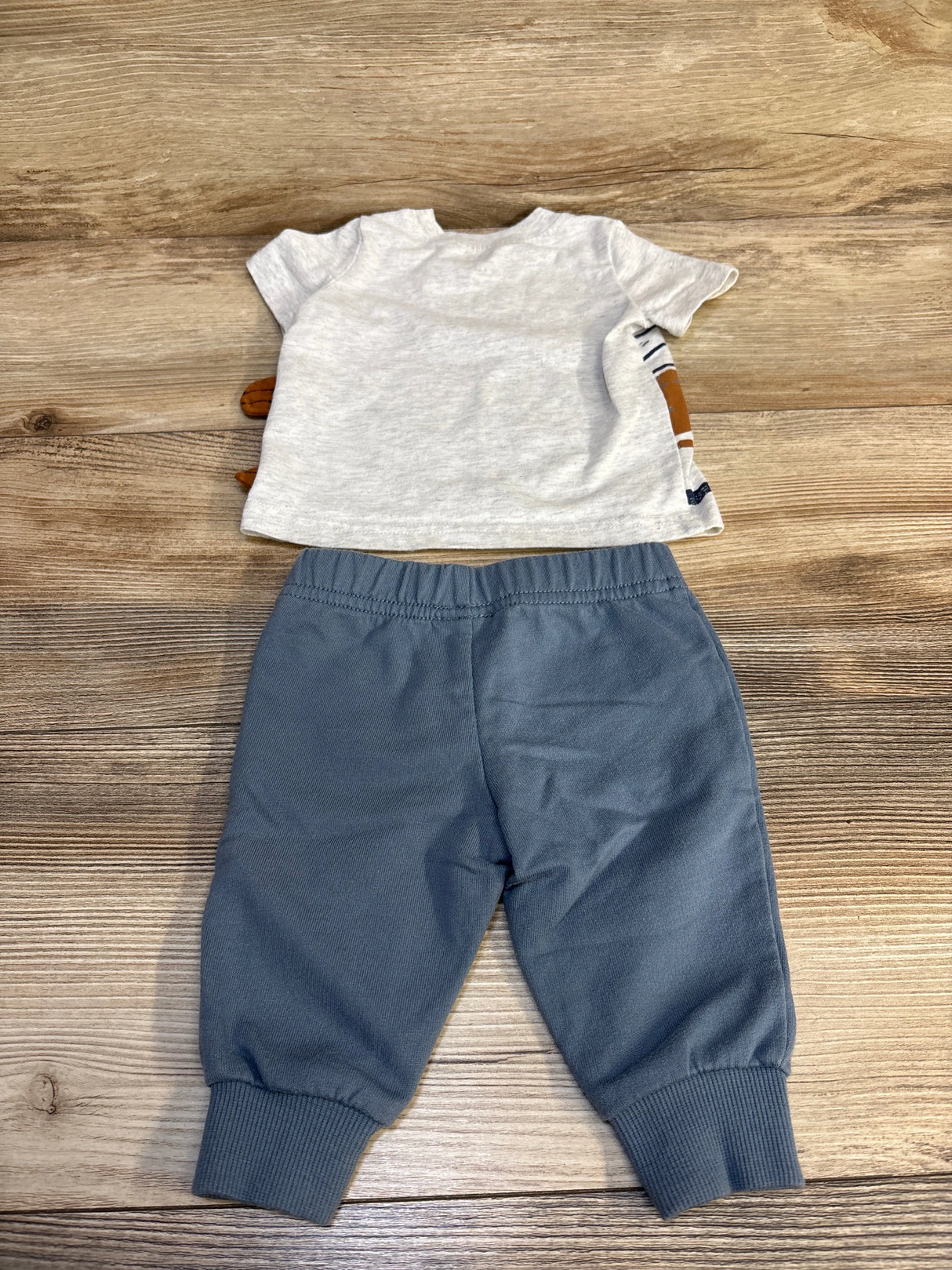 Light gray short sleeve baby shirt with blue jogger pants on wood background