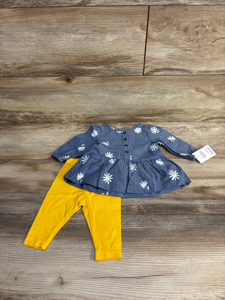 Baby outfit with blue long-sleeve top with white flower prints and yellow leggings on wooden floor