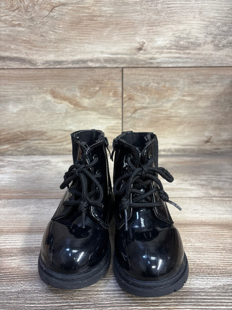 Front view of toddler black patent faux-leather lace-up ankle boots on wood floor showing round toes and laces