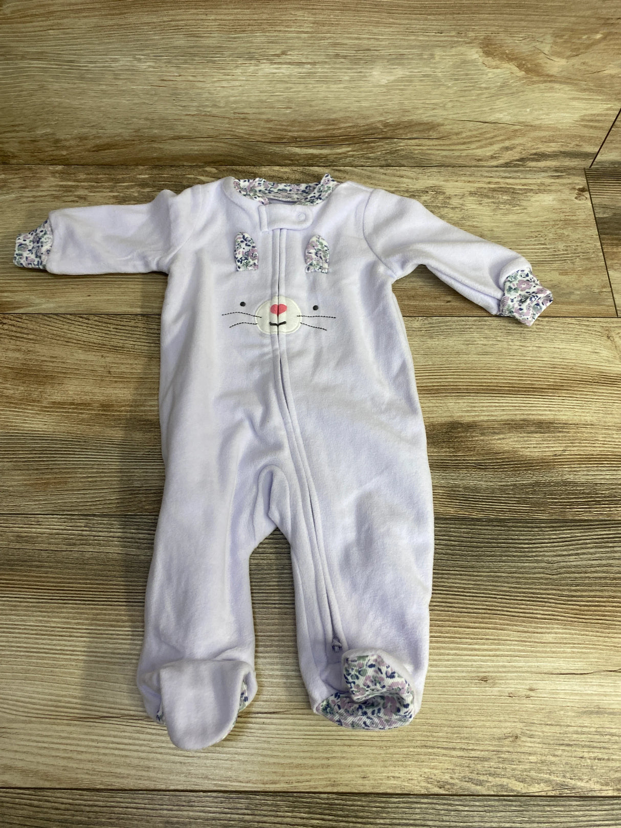 Light purple baby onesie with bunny face and floral trim on feet, cuffs, and collar on wooden floor