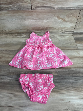 Flat lay of pink floral baby dress and matching bloomers showcasing daisy print and ruffled sleeves on light wood background