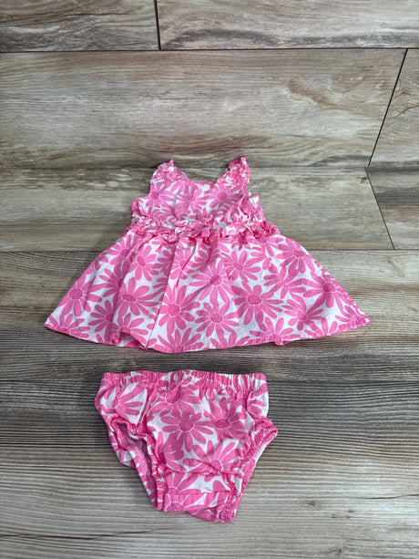 Flat lay of pink floral baby dress and matching bloomers showcasing daisy print and ruffled sleeves on light wood background