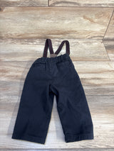 Back view of black suspender pants, 9M, with elastic waist, faux back pockets and red-striped suspenders on light wood floor