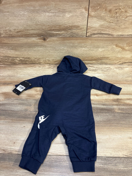 Back view of navy Nike hooded coverall showing white swoosh on left leg, attached hood and tag on wood floor background