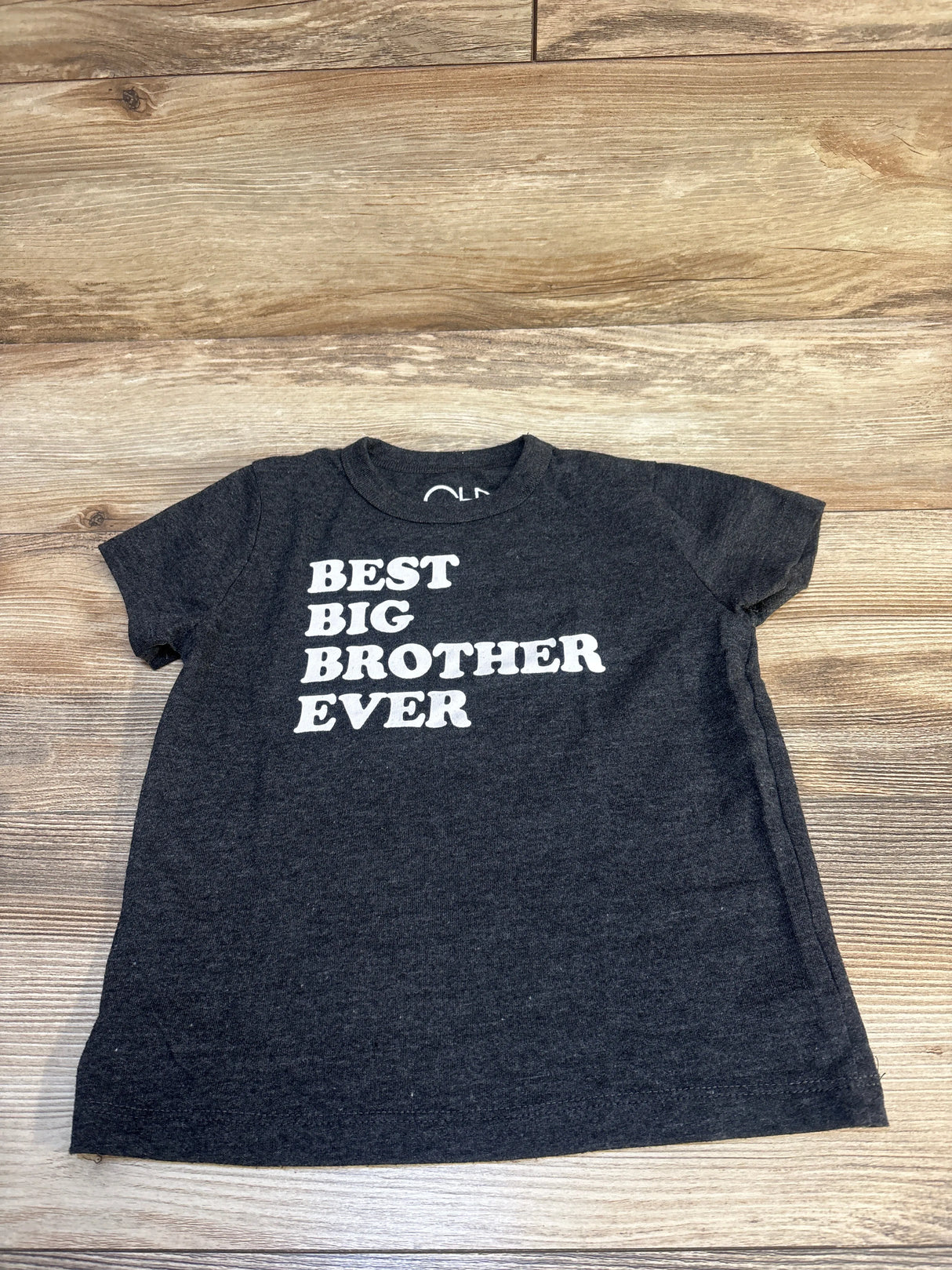 Black toddler t-shirt with 'Best Big Brother Ever' white text, laid on wood floor