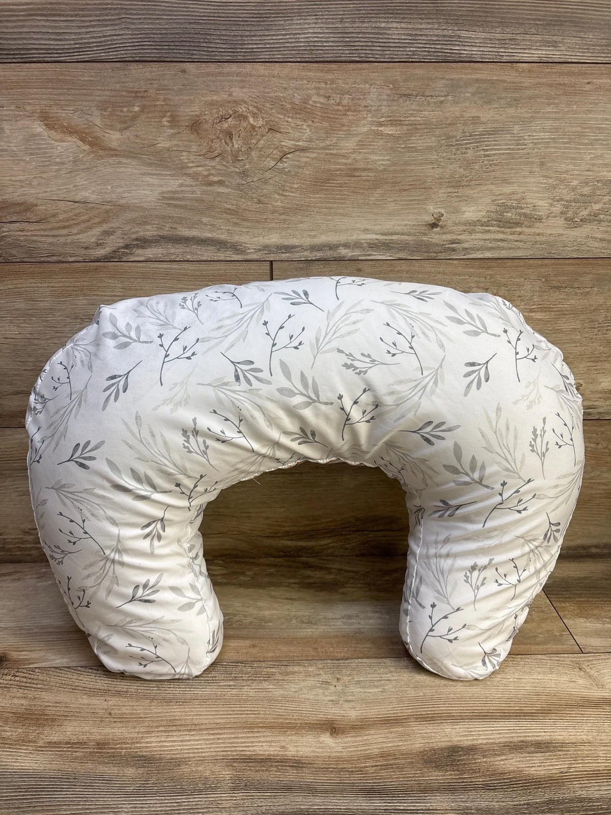 Top view of Boppy nursing pillow with botanical leaf slipcover showcasing its U-shaped design on a wood background