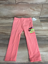 Flat lay of toddler pink Nike leggings size 4T showing stacked multicolor NIKE logo on right leg on wood floor background