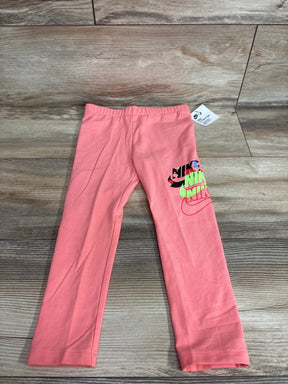 Flat lay of toddler pink Nike leggings size 4T showing stacked multicolor NIKE logo on right leg on wood floor background