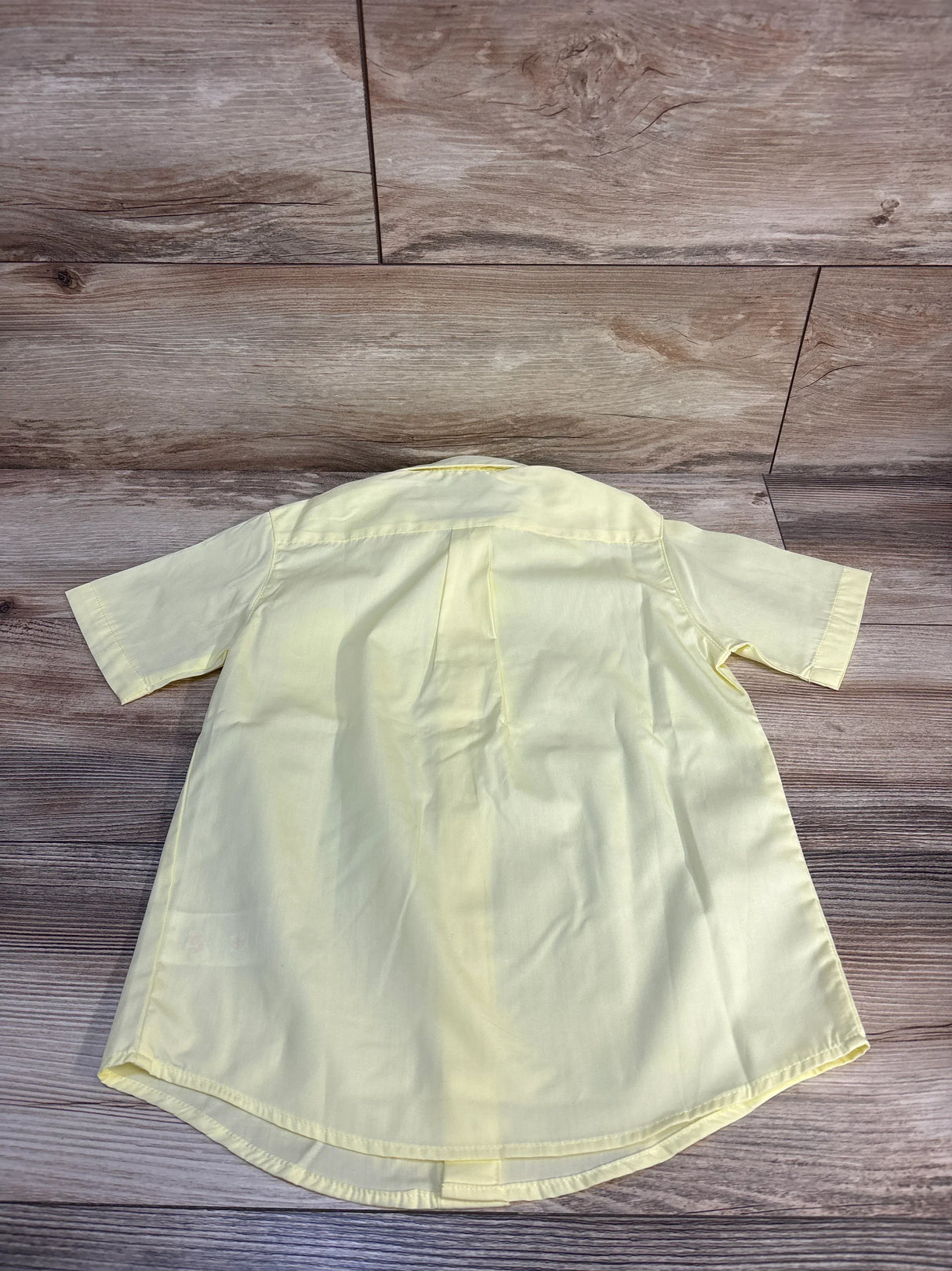Light yellow kids short sleeve button-up shirt on wood floor, ideal for baby or toddler clothing resale