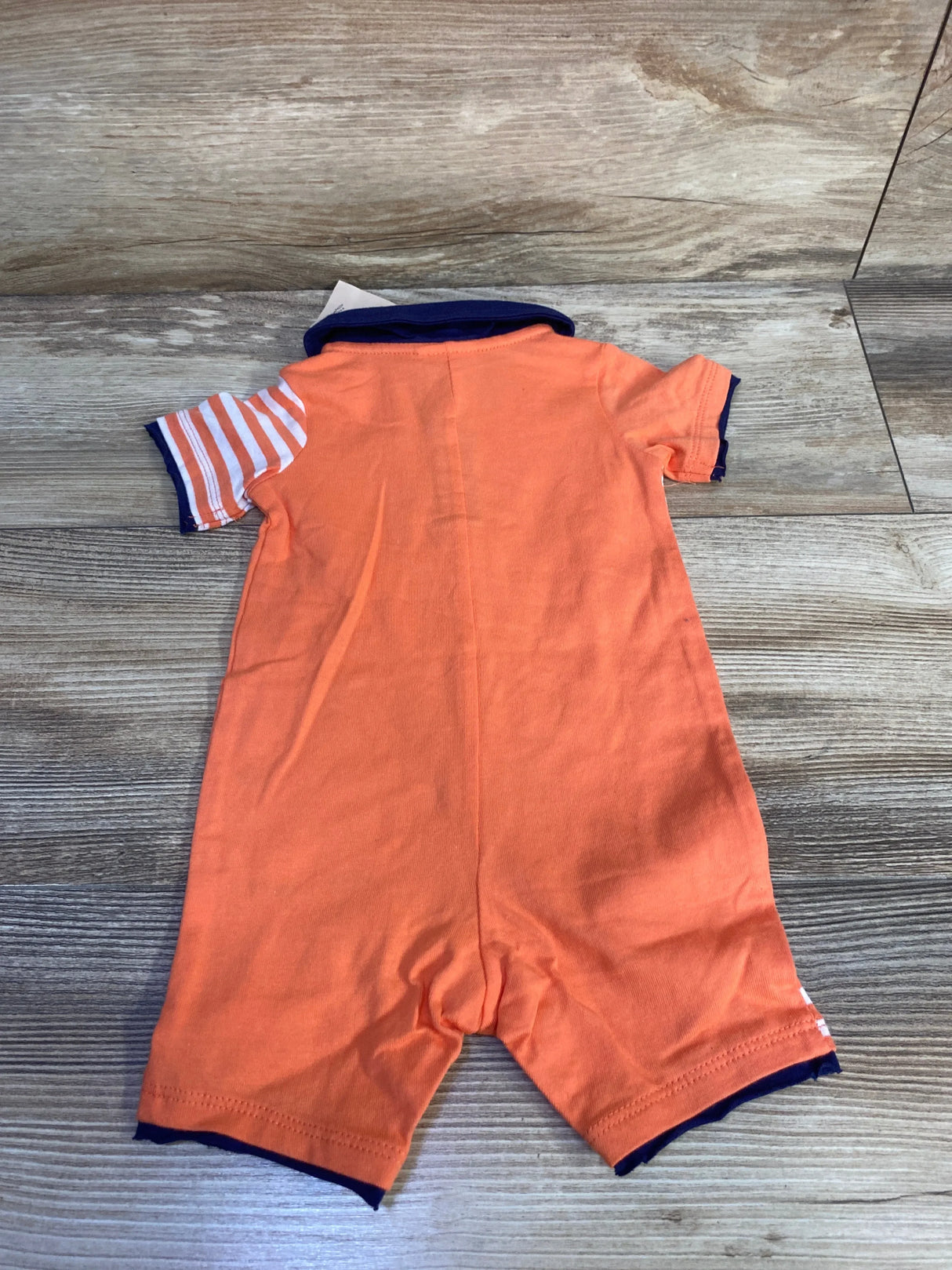 Back view of orange shortie polo romper (0-3M) showing navy collar and cuffs and striped sleeve on wood background