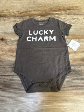 Flat lay of Face To Face Lucky Charm bodysuit in grey with white text print and hangtag attached on wood plank floor