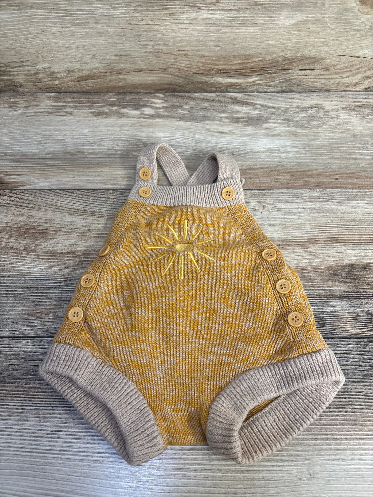 Flat lay of beige knit baby bubble romper size 6 months showing embroidered sun, wooden buttons and ribbed cuffs on wood background