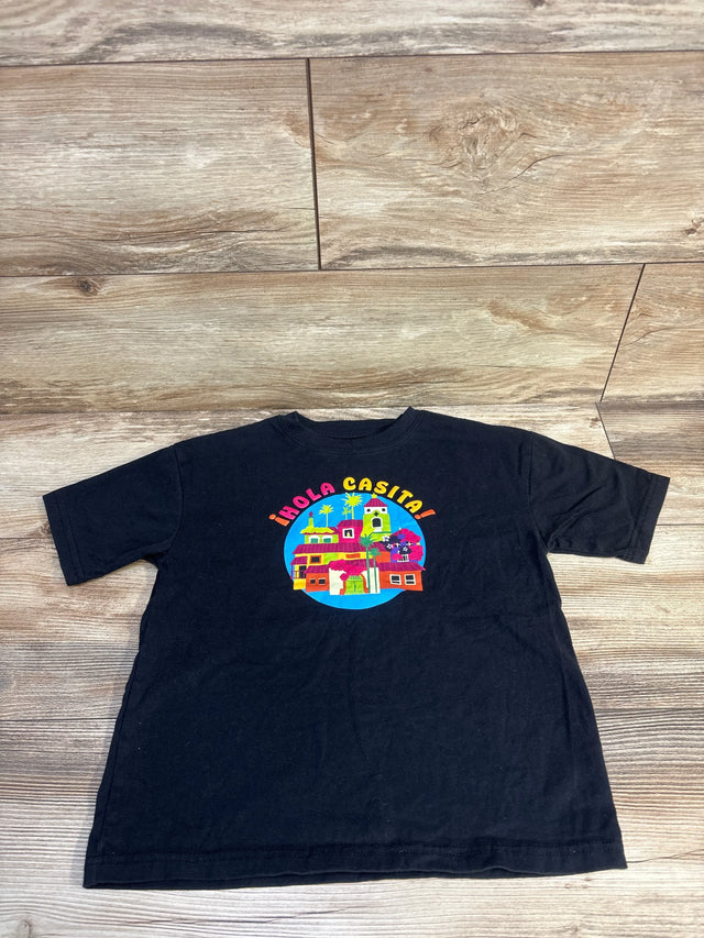 Black kids t-shirt with colorful '¡Hola Casita!' village graphic, laid on wood floor
