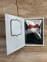 Angled view of white formal baby onesie with pinstripe vest print and red polka-dot bow tie tied with sheer ribbon in gift box on wooden table