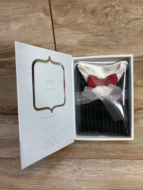 Angled view of white formal baby onesie with pinstripe vest print and red polka-dot bow tie tied with sheer ribbon in gift box on wooden table